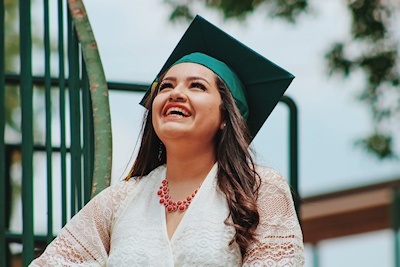 A woman wearing a graduation cap smiling and looking at the sky.