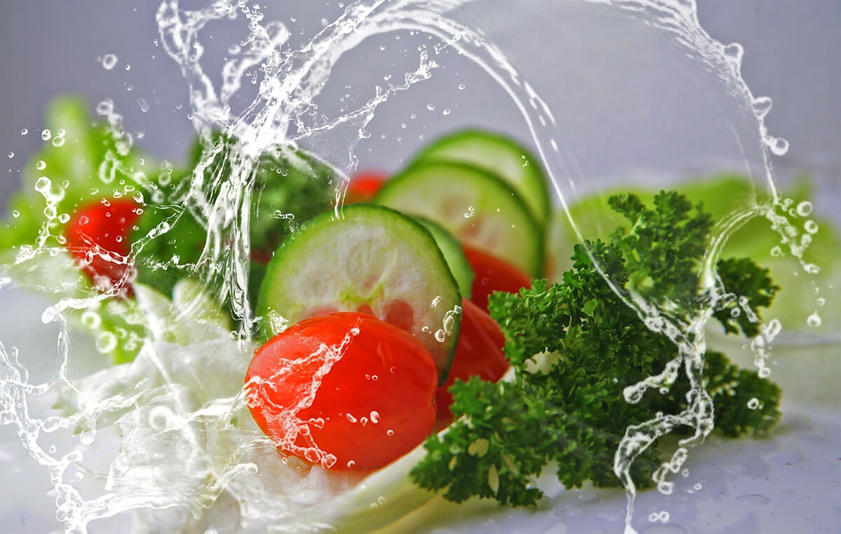 The picture shows a variety of green colored foods combined in a salad.  A splash of water over the food highlights the image.