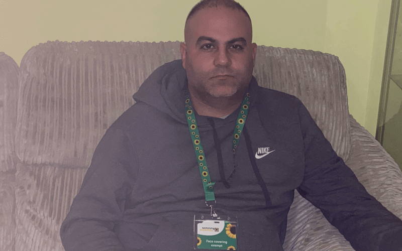 Marco Naayem sitting on a sofa wearing a sunflower lanyard