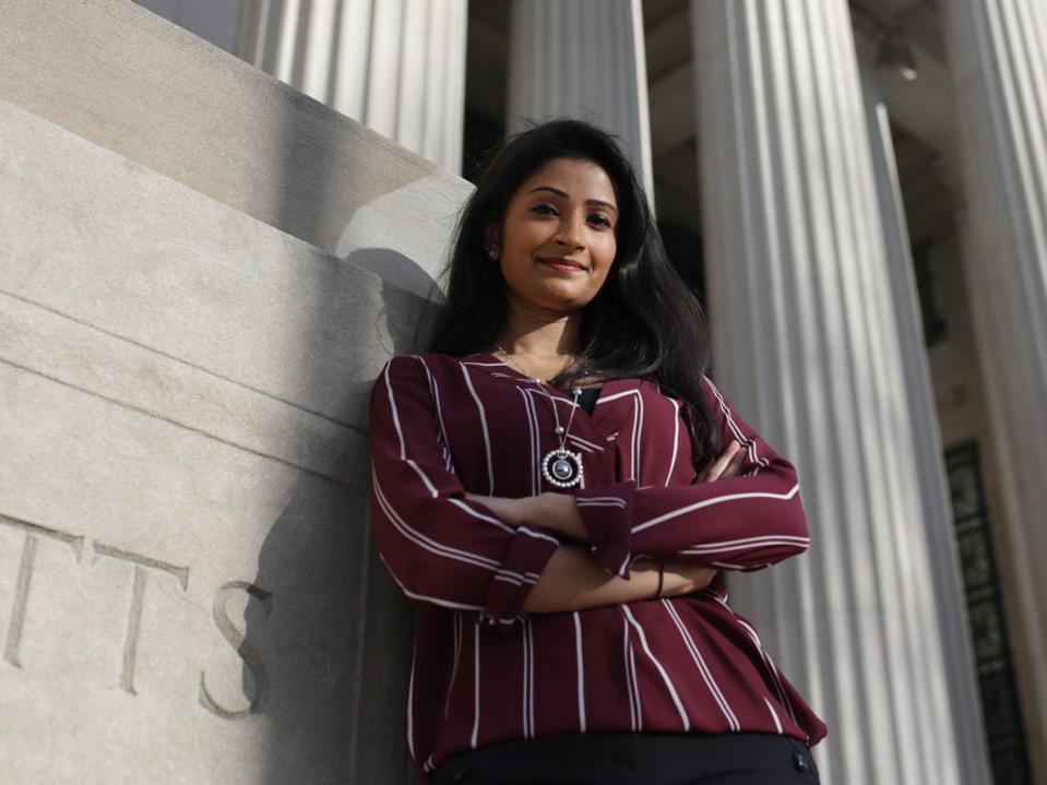 Shriya Srinivasan showed standing, smiling, leaning against an MIT building with pillars.
