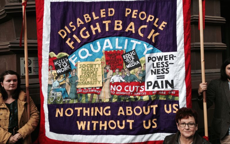Tapestry featuring rights slogans such as Disabled People Fight Back and Nothing About Us Without Us