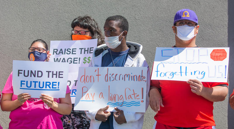 Four people, all wearing masks, stand holding signs that read