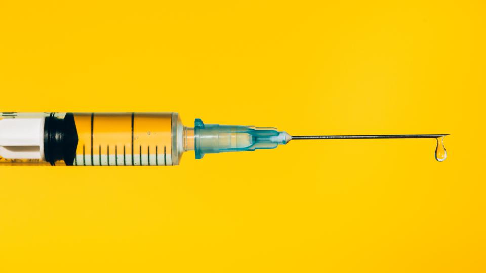 Modern syringe with liquid drug, pictured against a plain yellow background.