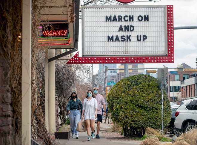 Juan Tenorio and his daughters Abagail, 20 and Isabel, 18, walk past a sign inviting people to mask in Austin on Tuesday, the day before the end of a nationwide masking mandate.