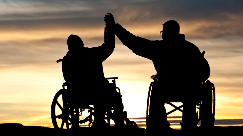 Silhouette of two wheelchair users high fiving with sunset in the background